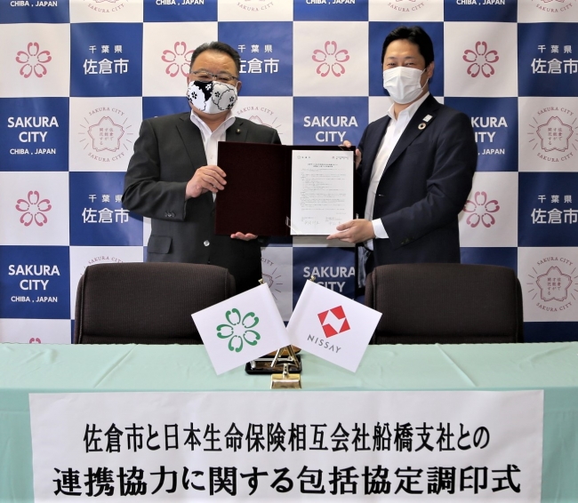 署名済の協定書を掲げる西田佐倉市長（左）、日本生命中山支社長（右）